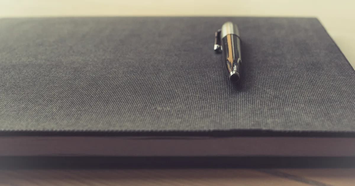 Pen on a notebook beside a laptop while drafting stronger resume bullet points.